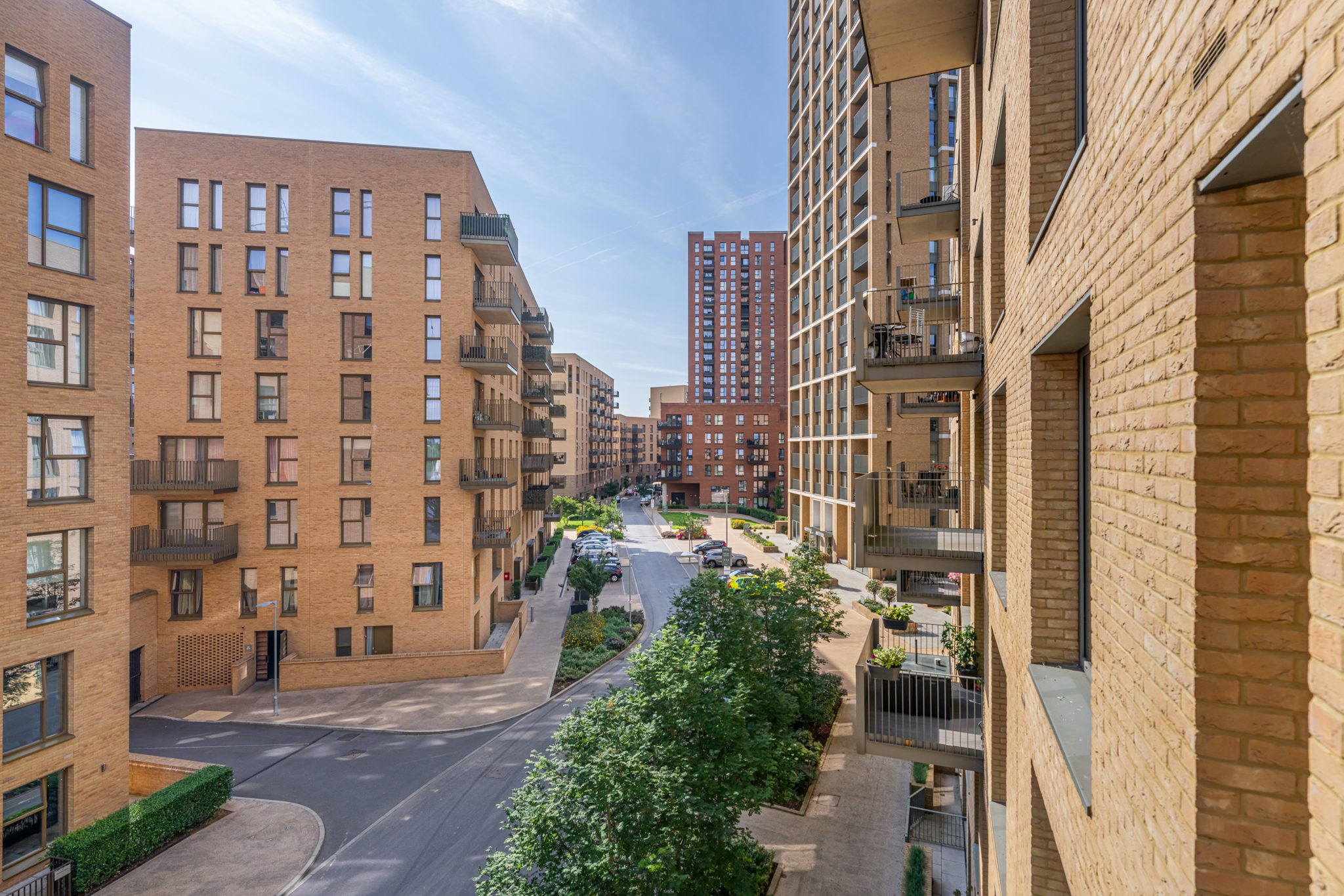 Balcony view across a modern apartment development with brick buildings and landscaped courtyard