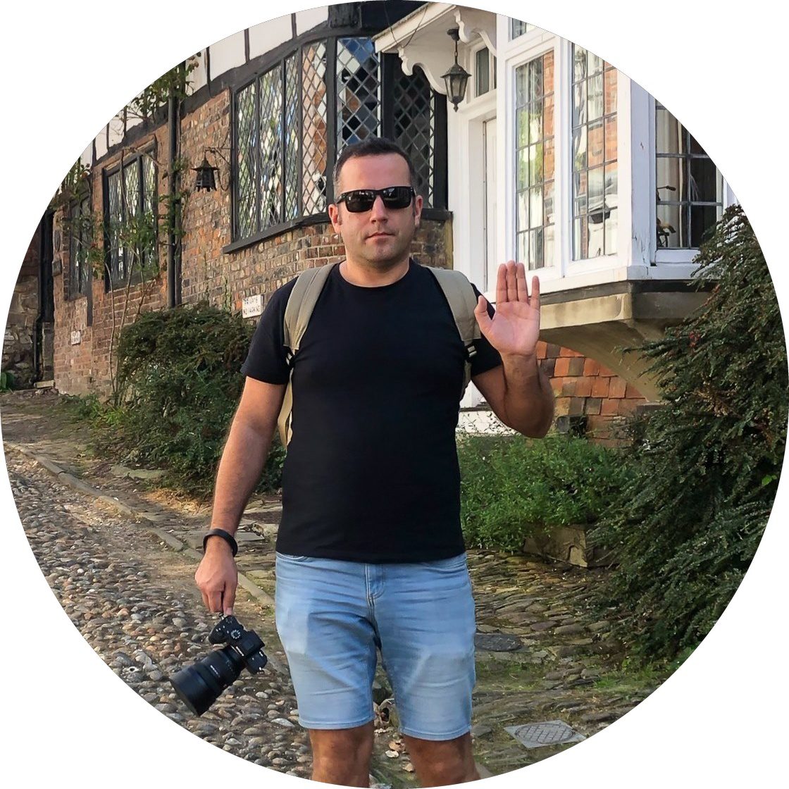 Valdis, owner of Ambershore Pix, holding a camera on a cobbled street with historic houses